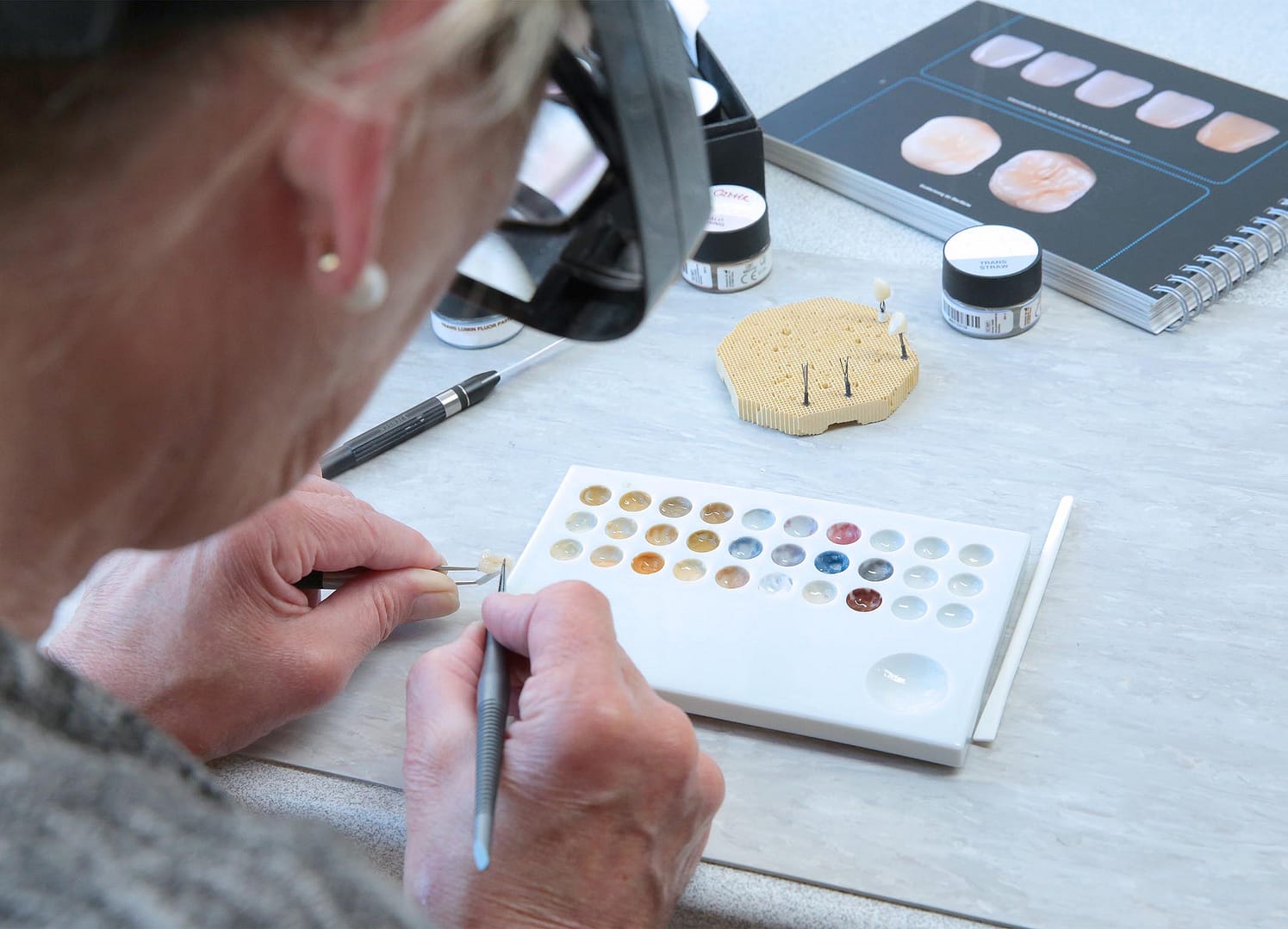 Detailarbeit an einem Zahn, Zahn mit Zange in der Hand einer Zahntechnikerin